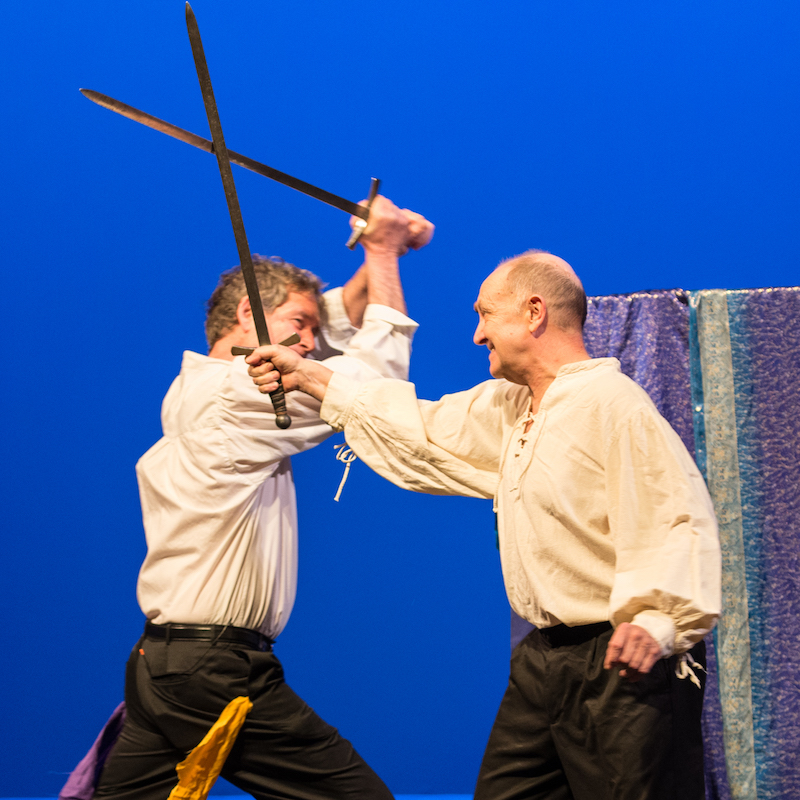 Actors David Zucker and Richard McElvain with mouths agape imitating a skull held by David, in front of a Shakespeare book
